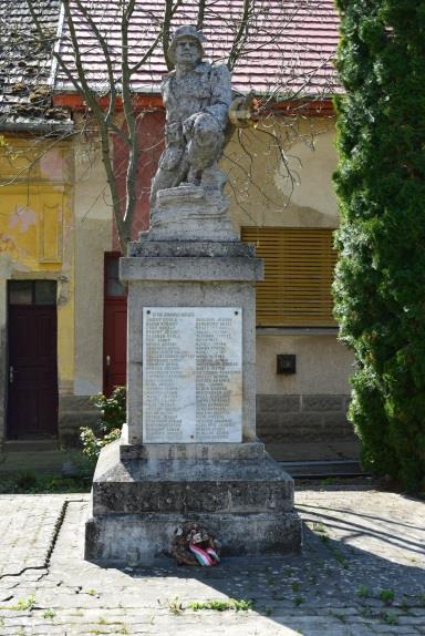 hasábszerű posztamensre helyezett páncélsisakos katona kőből faragott szobra.