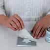 2) Permetezze be a mylar egyik oldalát egy vékony réteg ragasztóval, majd nyomja rá a fóliát a képeslapra. Fújja rá a festéket.