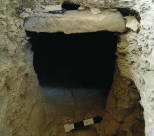 A tengely folyosójának végén, arra merőlegesen, aknaszerű (2 x 1 m), de szabálytalan lépcsőkkel kialakított lejárat vezet balra, nyugatra, ahol alacsony, befelé lejtős plafonnal (~115 x 90 cm),