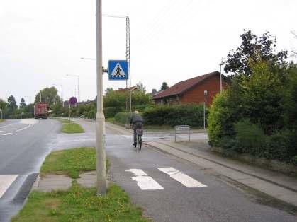 Kerékpárút lakott területen 60 km/h, nagy forgalom és emelkedő: Széles kerékpárút (mindkét oldalon) és széles, füvesített elválasztósáv.