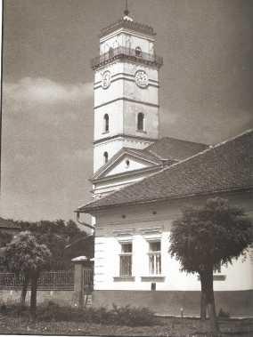 8. kép. Templomtorony Kunmadarason, vasrácsos galériával, (előtérben a paplak). Forrás: Kútvölgyi Mihály: Tűzre, vízre vigyázzatok! - tűztornyok, tűzoltóemlékek. (Colorplast, 1989. Békéscsaba. 60.