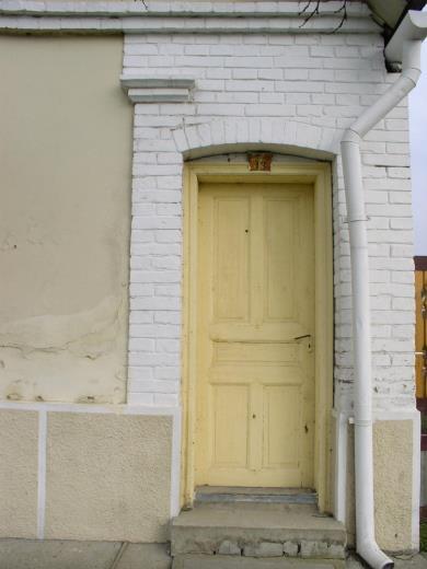 Az íves záródású faragott ajtót fehérre festett, téglamintázatú falrész övezi.