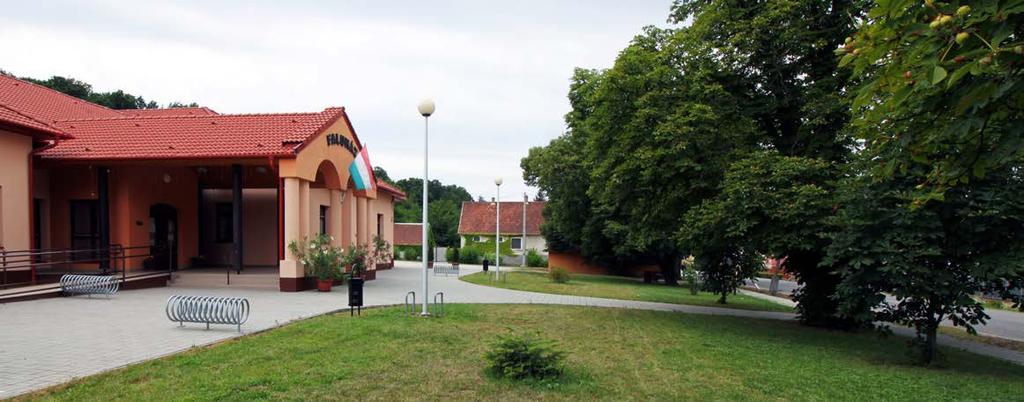 A Faluház előtti teret a főúttól koros vadgesztenye fasor választja el.