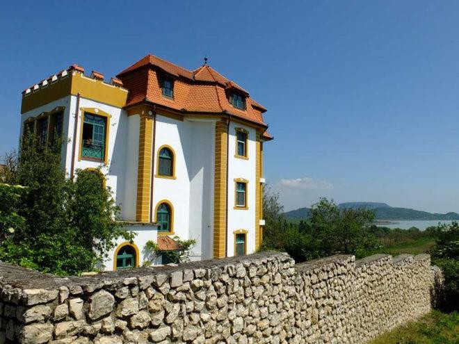 Az Újhegy lábánál, a 053 hrsz ingatlanon áll a háromszintes eklektikus épület, amely a Balaton felé nyíló panorámát helyezi fókuszpontba.