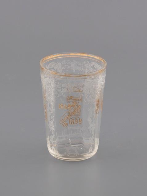 113. Jubileumi pohár / Emlékpohár Formába fújt színtelen üveg aranyozással és savmaratott díszítéssel.