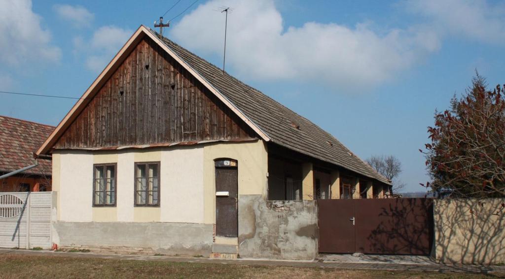 49 Az alábbi képen a bemutatott ablakokon túl ismét az oly jellemző elemeket láthatjuk, a klasszikus deszkás oromzatot, az oszlopos tornácot - ajtóval az utcára,