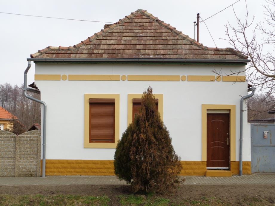 Az épülettel azonos színű falazott kerítésbe beépített kovácsoltvas kapu is hagyományőrző, az udvarra való betekintés lehetősége barátságosabbá teszi az utcaképet.