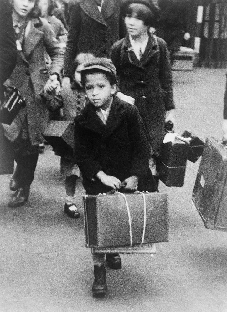 Evakuáltak Egy bőröndjét cipelő kisfiút ábrázoló fénykép, amint más evakuáltakkal együtt 1940. július 5-én Londonból vidékre indul.